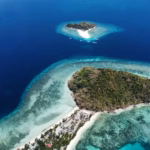 Wide aerial drone view of two tropical islands separated by a vibrant turquoise coral reef system in deep blue ocean waters in Palawan.