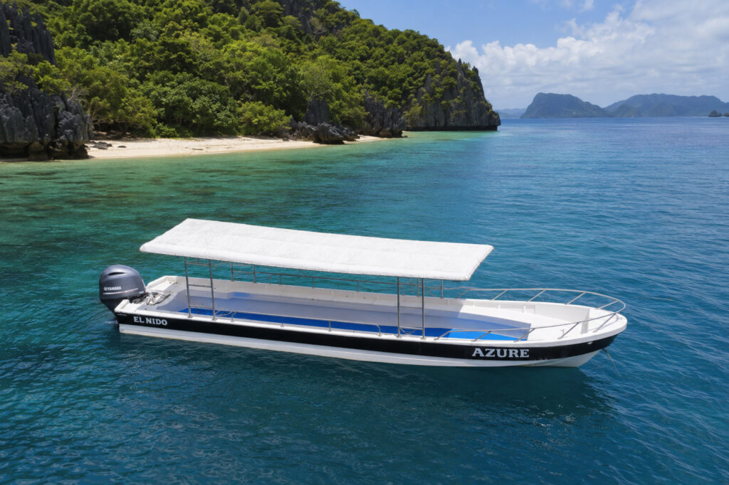 Fotografia em alto ângulo de um longo barco branco chamado Azure com um dossel branco ancorado em água turquesa perto de uma praia da ilha em El Nido.